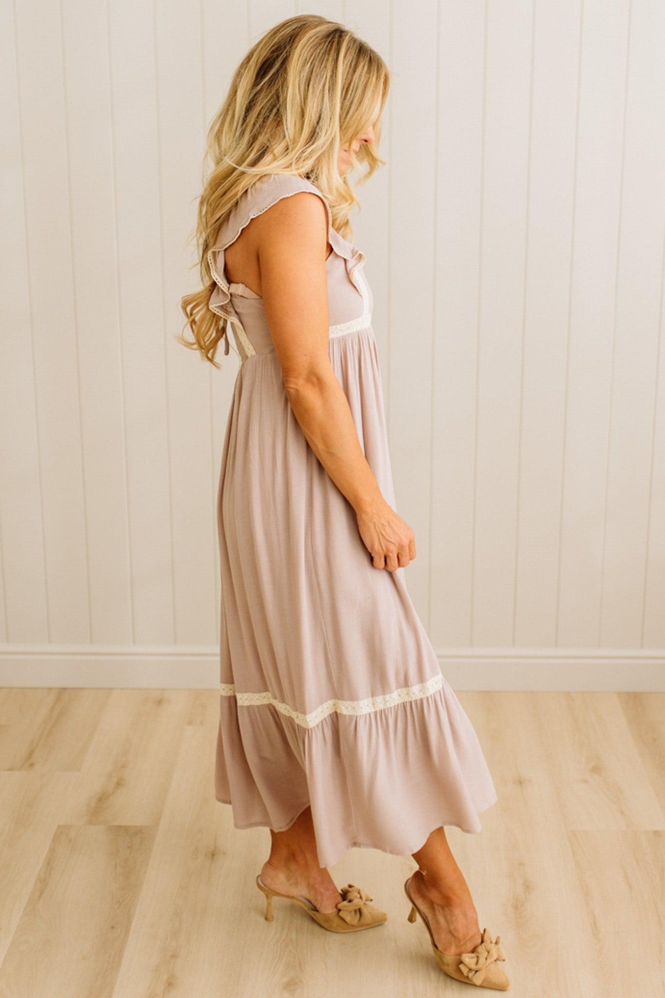 Woman wearing a light pink dress with white trim in a room with wooden flooring and a white wall.