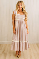 Woman wearing a long, light-colored dress with a white top against a wooden paneled wall.