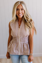 Blonde woman wearing a mocha and white gingham print sleeveless top with smocked waistline and centered gold zipper front.