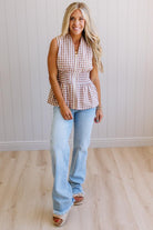 Blonde woman wearing a mocha and white gingham print sleeveless top with smocked waistline and centered gold zipper front.