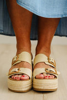 Person wearing beige sandals with a platform on a light wooden floor.