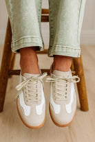 Person wearing beige sneakers with white soles on a wooden stool.