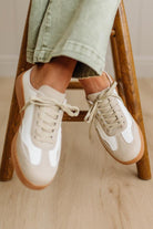 White and beige sneakers worn by a person sitting on a wooden stool.
